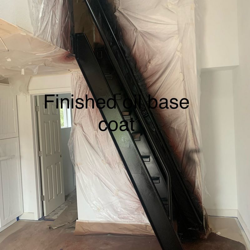 Black staircase beam leaning in a room, wrapped in plastic, with text “Finished base coat” overlaid