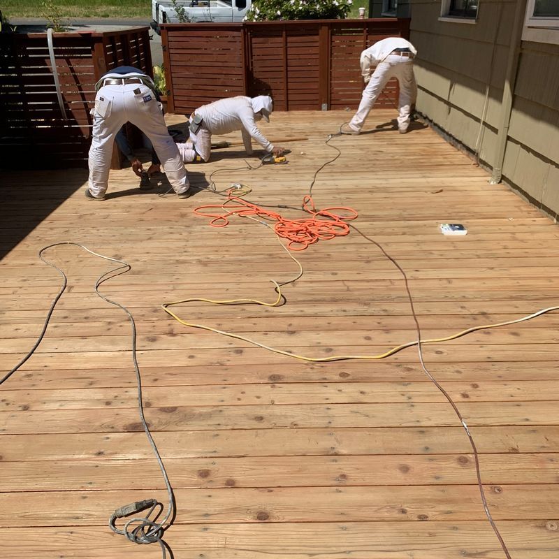 Three workers installing a wooden deck, with orange extension cords spread across the boards.