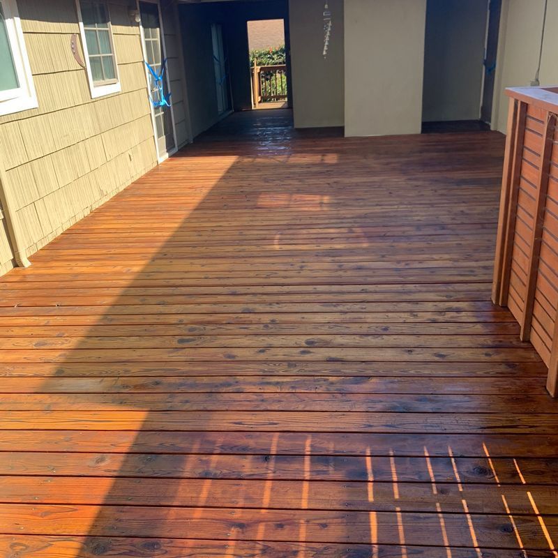 Wooden deck walkway beside a house, with sunlight and shaded areas leading to a doorway.