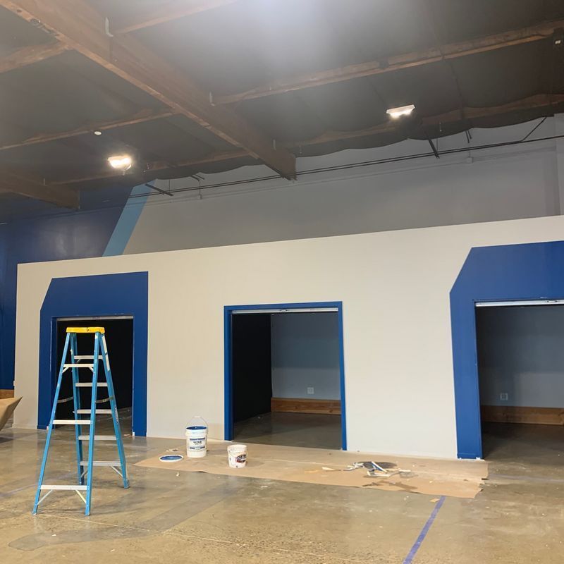 Blue-doored interior wall under construction with a ladder, paint bucket, and tools on the floor