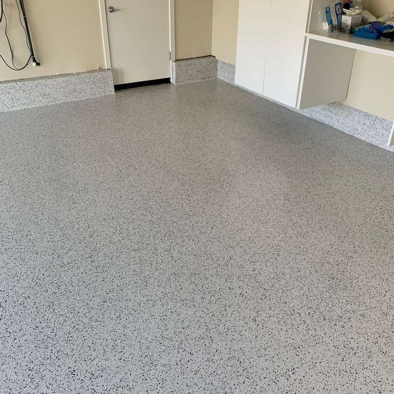 Empty garage with gray speckled epoxy floor and built-in cabinets along the wall