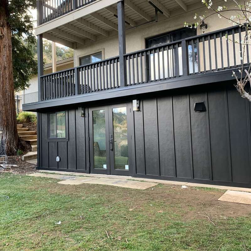 Dark gray house exterior with deck and railing above a ground-level door and windows