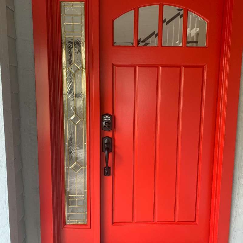 Bright red front door with a black handle and narrow decorative glass sidelights