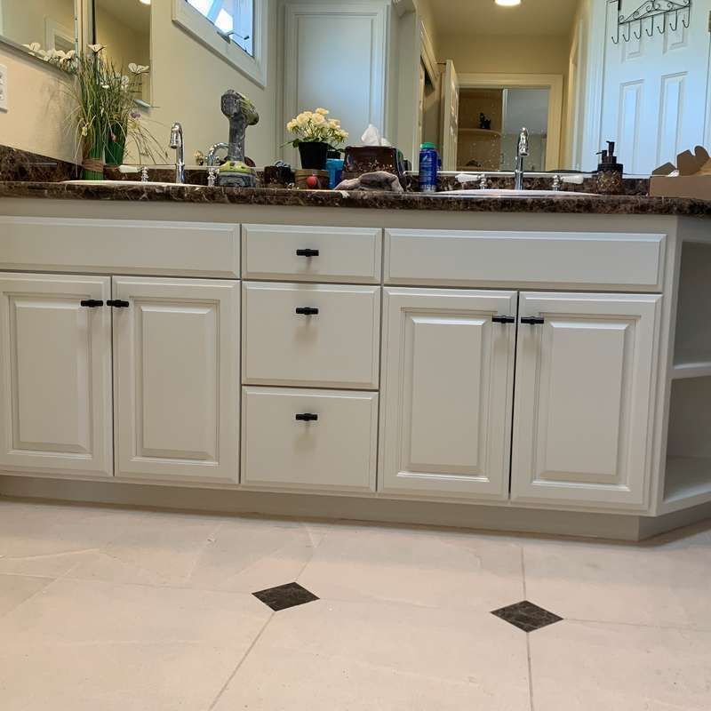 Bathroom vanity with white cabinets, granite countertop, mirror, and beige tile floor.