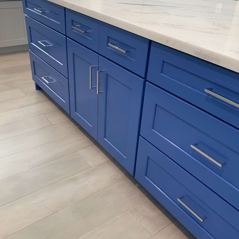 Blue kitchen cabinets with silver handles and a white countertop along a light wood floor