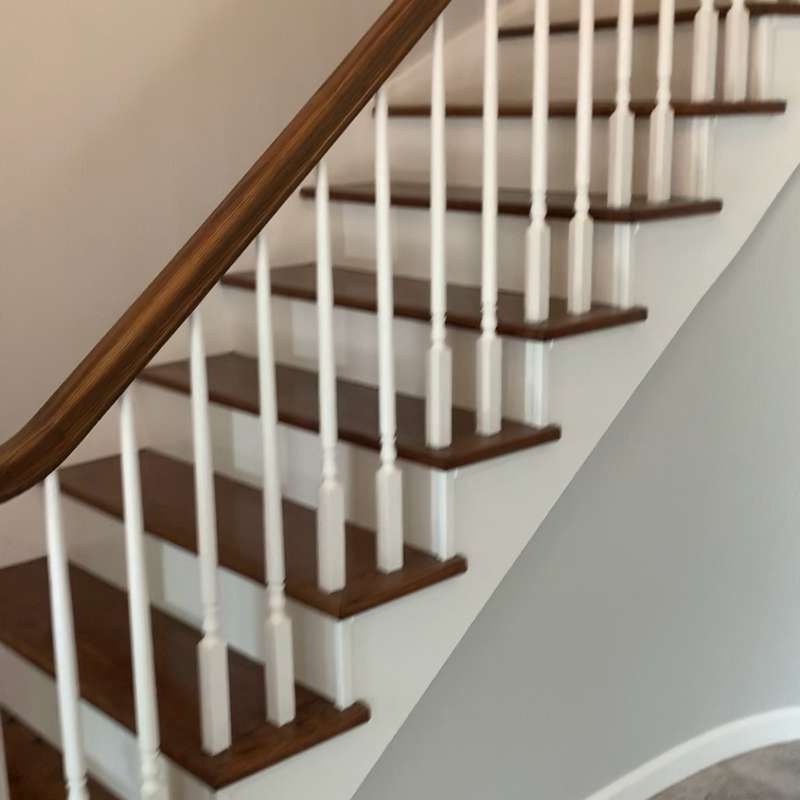 Wooden staircase with dark treads, white spindles, and a curved handrail in a light-colored interior.