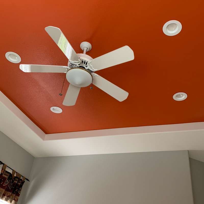 White ceiling fan on an orange ceiling with recessed lights in a room corner