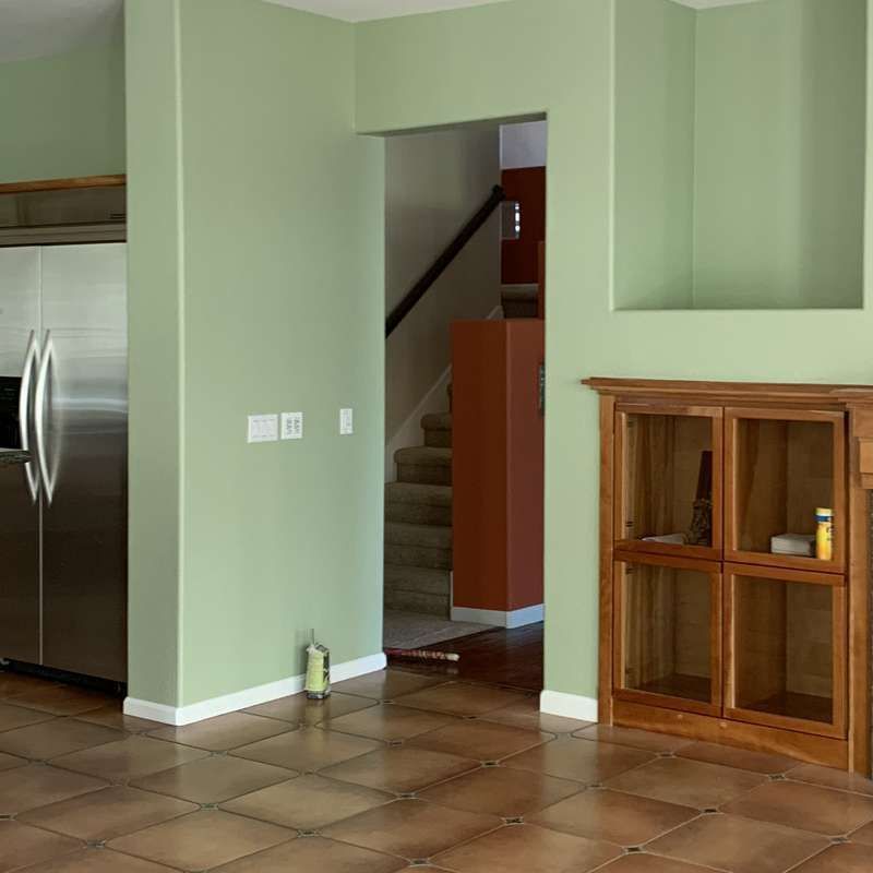 Empty kitchen with green walls, stainless fridge, tiled floor, and staircase visible through a doorway