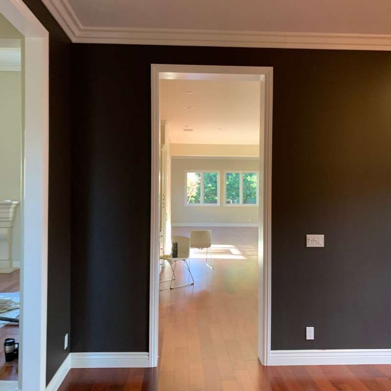 Empty room with dark brown walls, white trim, and a doorway opening to a bright room with a table and chairs.