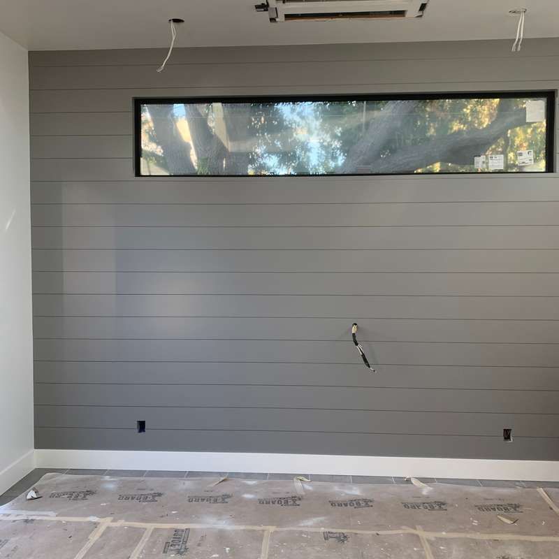 Empty modern room with gray accent wall, narrow window, and unfinished floor covering