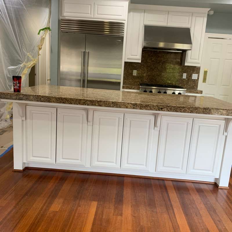 Modern kitchen with white cabinets, stainless steel appliances, granite island, and hardwood floors