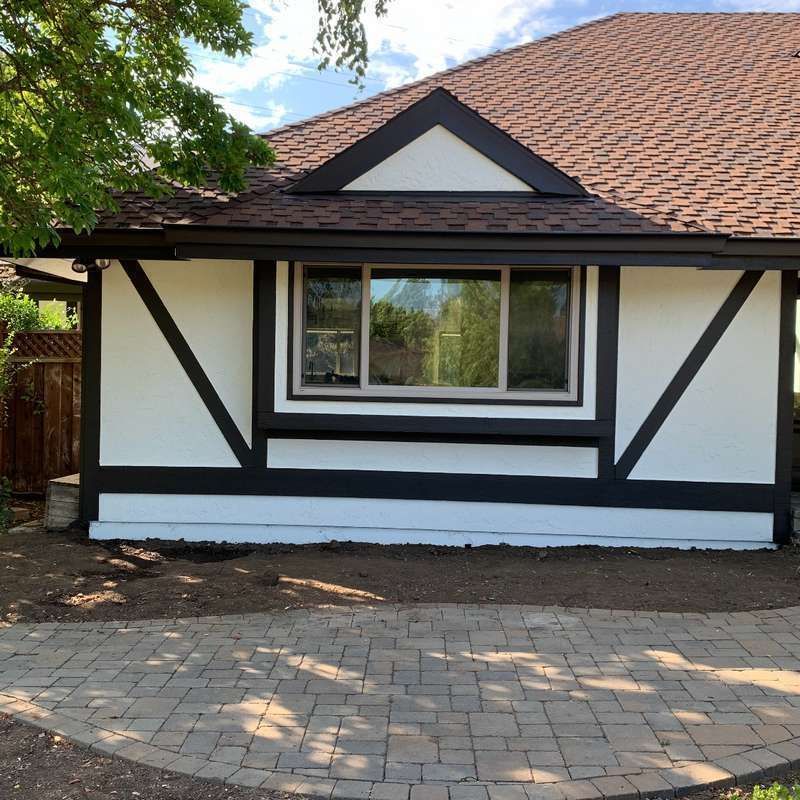 Front of a Tudor-style house with white walls, dark trim, a tiled roof, and a paved front path