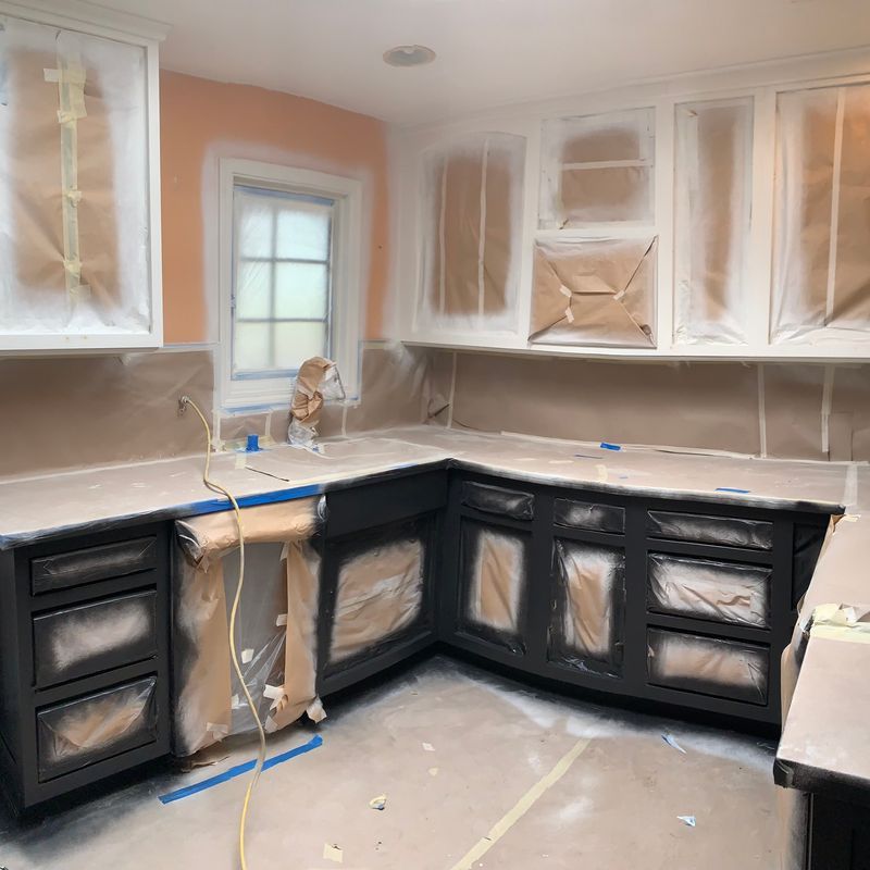 Kitchen under renovation with black cabinets, plastic-covered white uppers, and countertop prep work