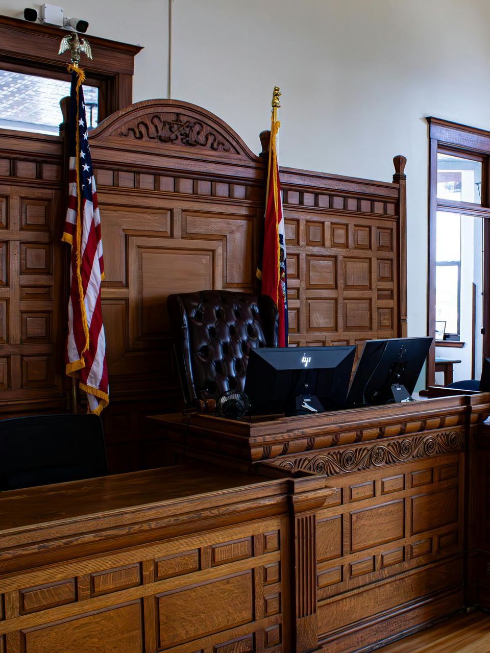 A judge 's bench in a courtroom with flags and a computer.