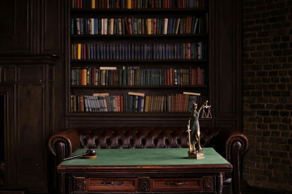 There is a statue of justice on a table in front of a bookshelf.