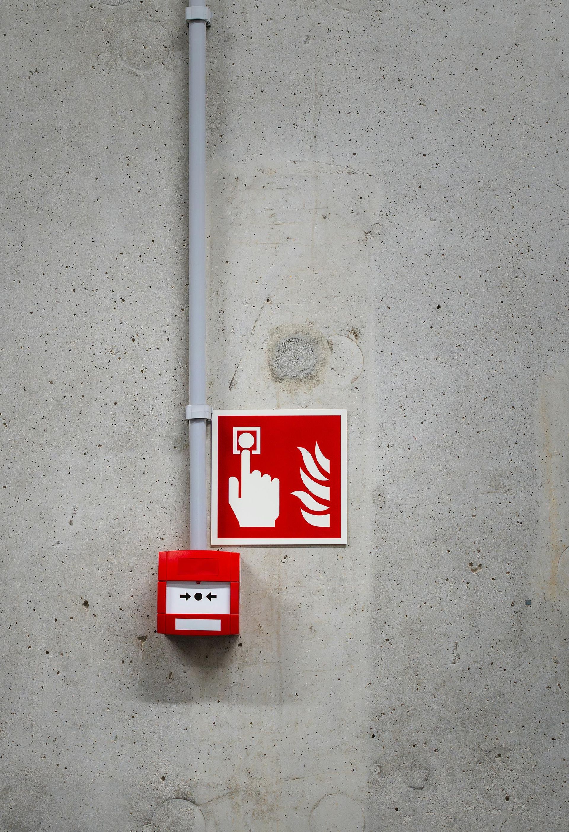Red fire alarm box and sign with a hand pushing a button on a gray concrete wall.