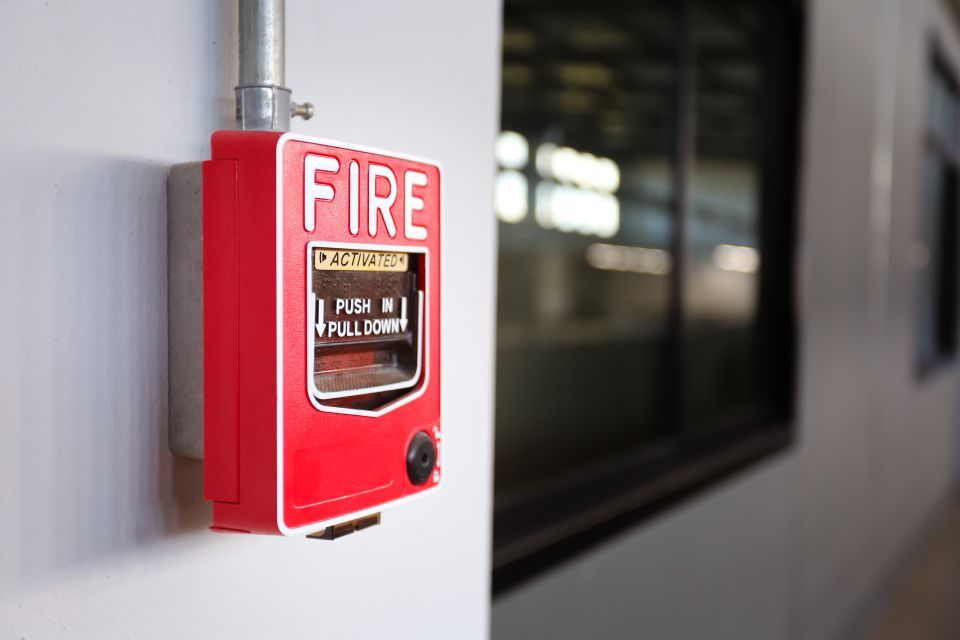 Red fire alarm box mounted on a white wall, near a window.