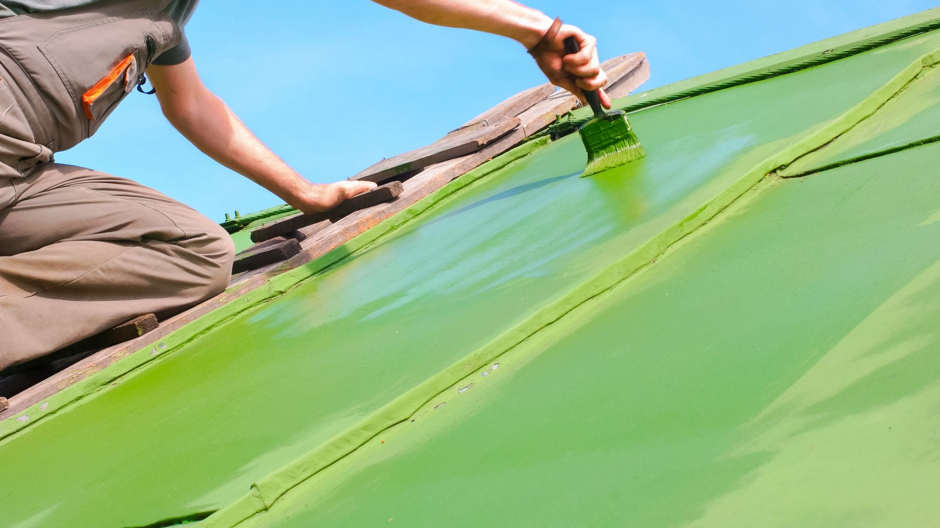 A man is painting a green roof with a brush.