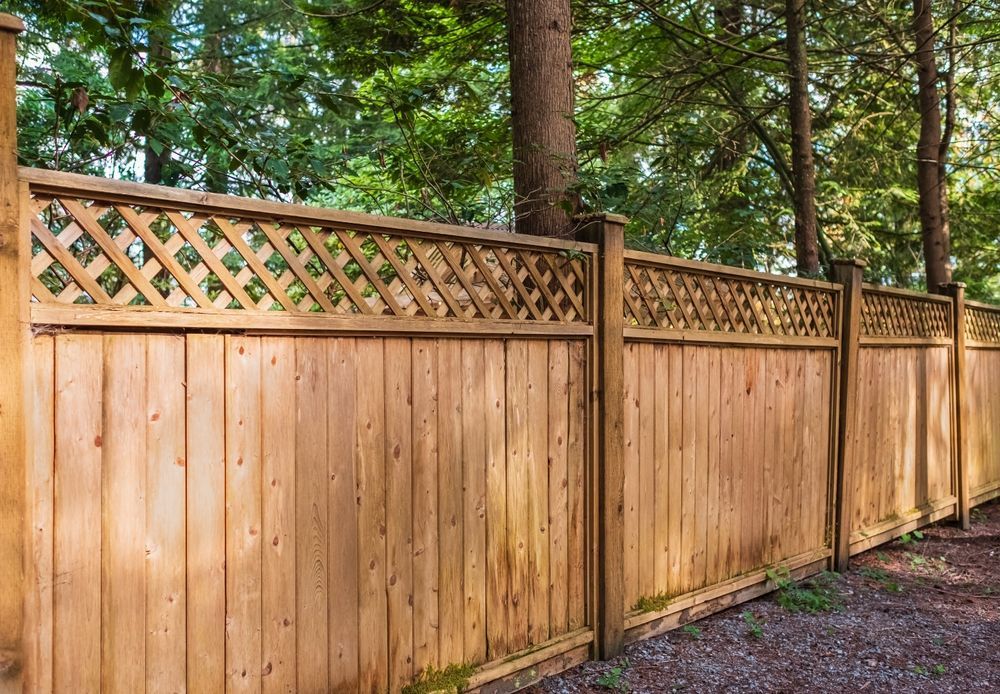 A wooden fence with a lattice design is surrounded by trees.