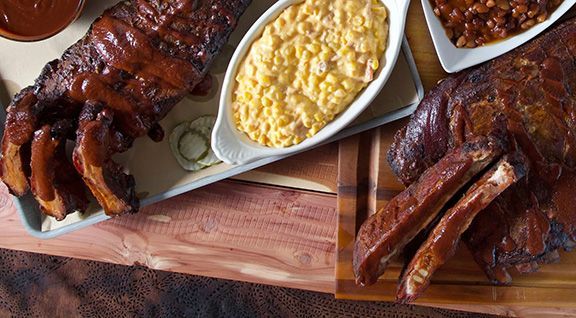 Smokehouse bbq kansas city wooden cutting board topped with ribs , macaroni and cheese , and beans.