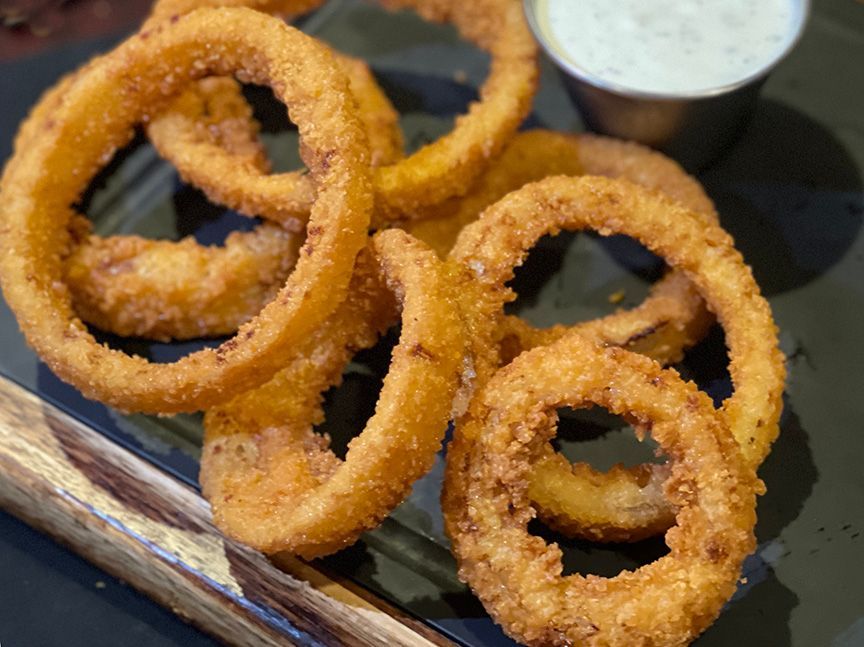 A plate of onion rings with dipping sauce and parsley in smokehouse bbq near Gladstone.