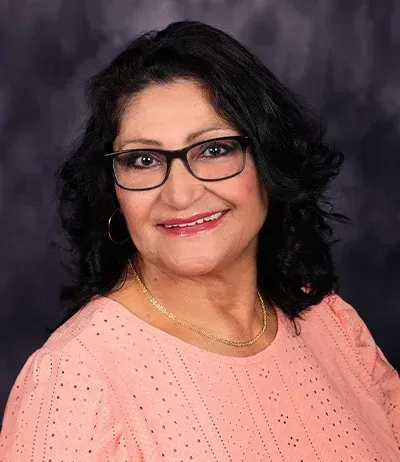 Woman wearing glasses smiling, wearing a pink shirt, in front of a dark blue background.