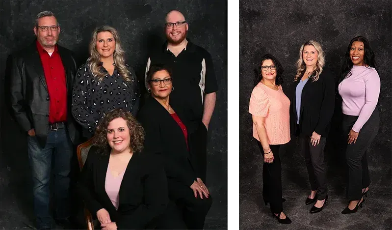 Group of six people posing for a photo. Three people stand, three sit or kneel in front. Dark background.