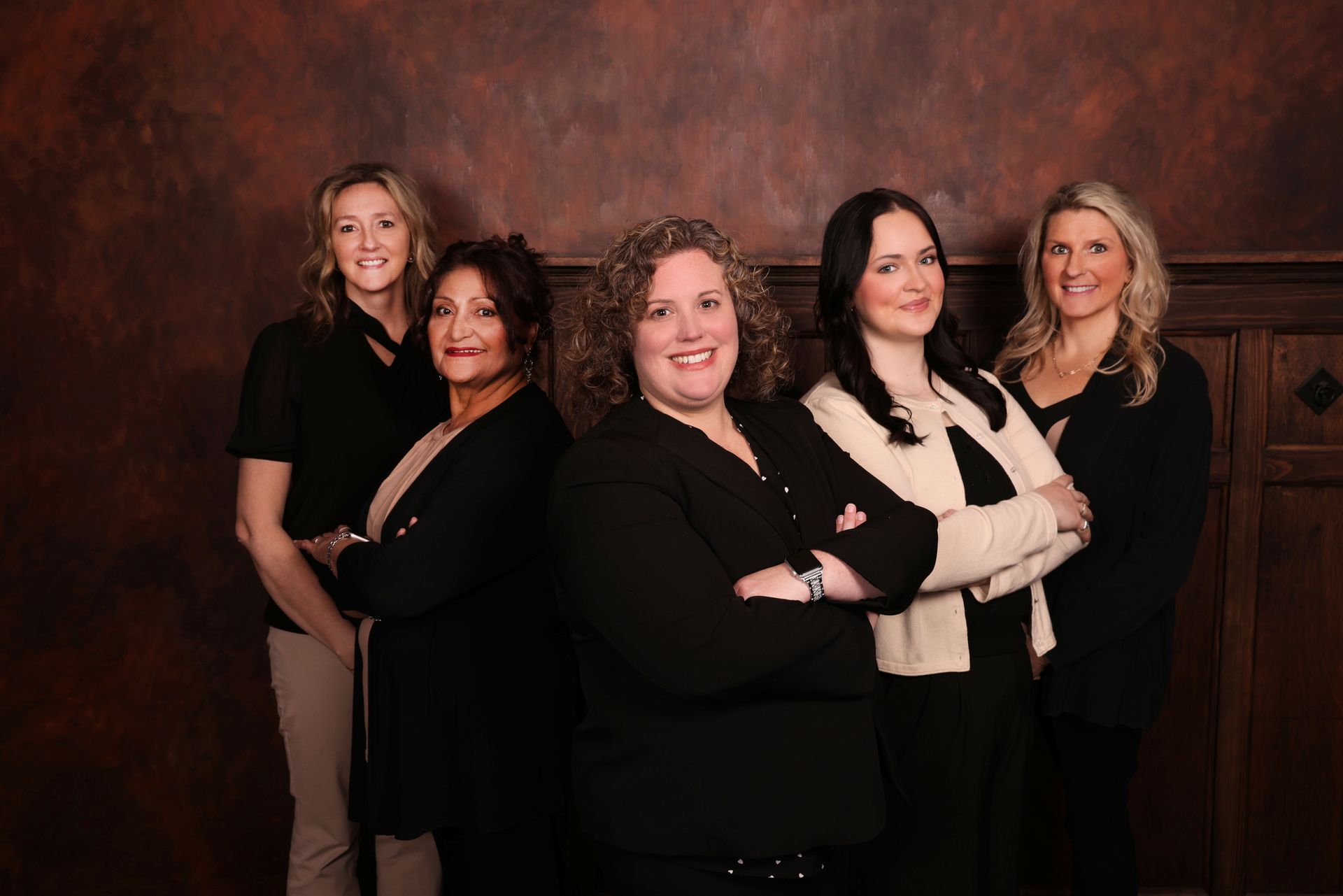 Group of six people posing for a photo. Three people stand, three sit or kneel in front. Dark background.