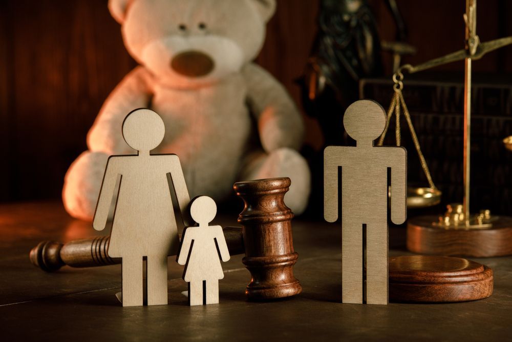Wooden family figures, gavel, scales, and teddy bear, suggesting legal matters involving a family.