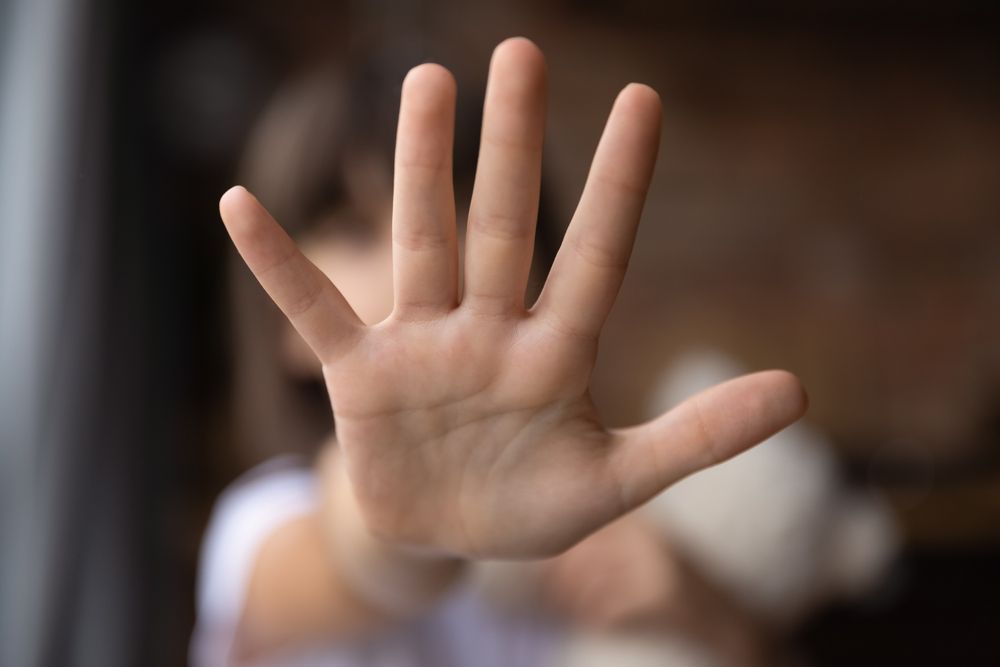 Child's hand outstretched, palm facing camera. Blurred background, white shirt visible.
