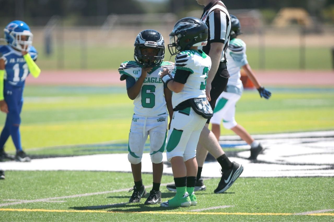 Football players in action on a grassy field; one runs with the ball, pursued by two opponents.