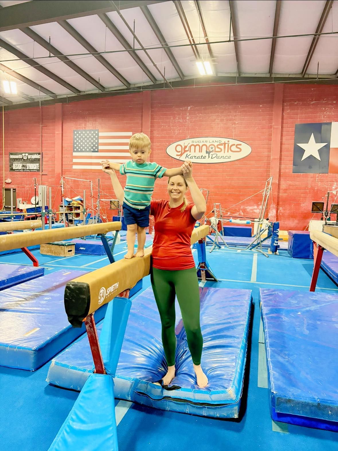A woman and a child are standing on a balance beam in a gym.