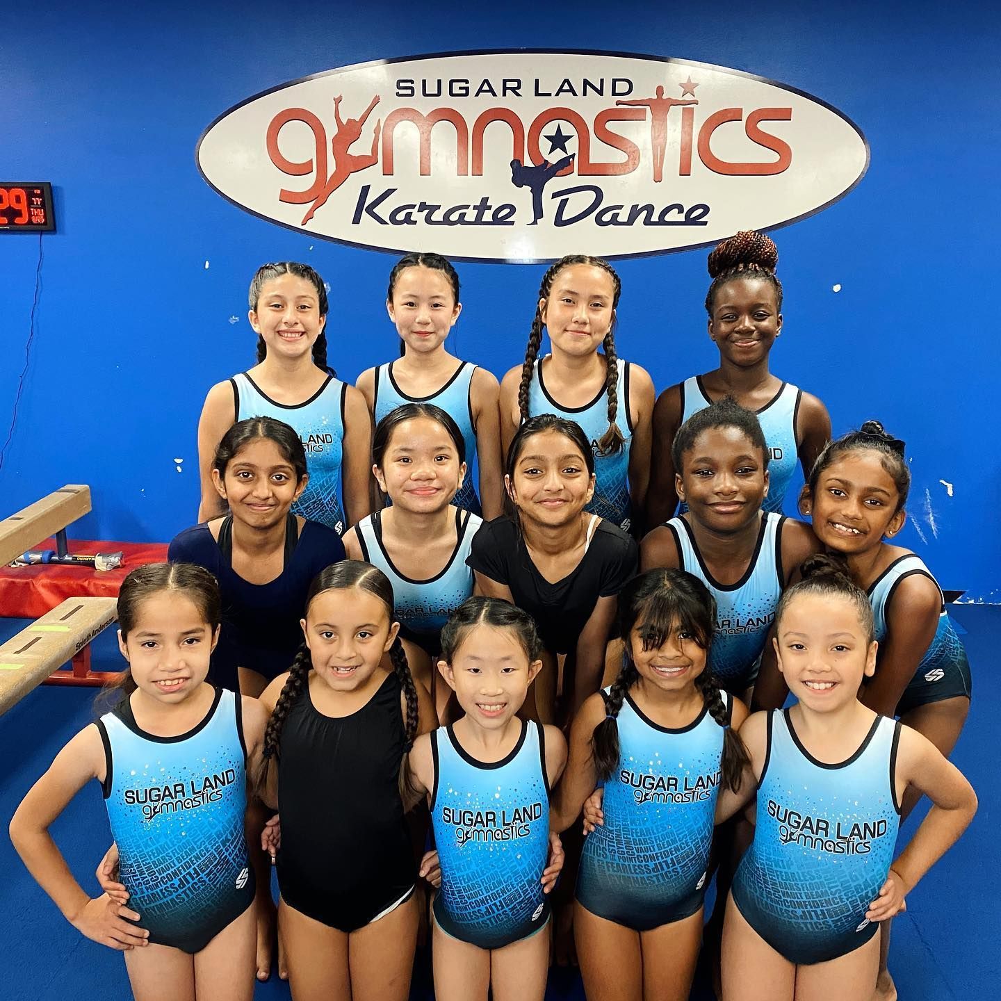 A group of young girls are posing for a picture in front of a sign that says sugarland gymnastics karate dance