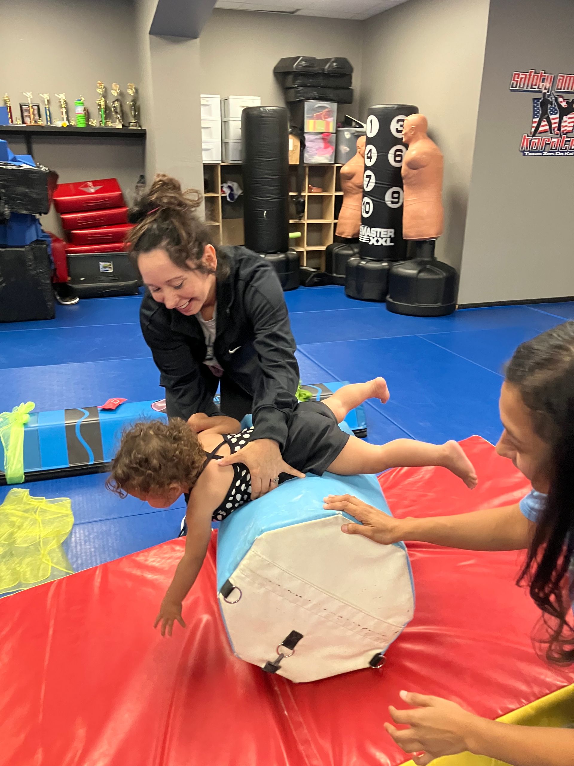A woman is playing with a child on a mat in a gym.