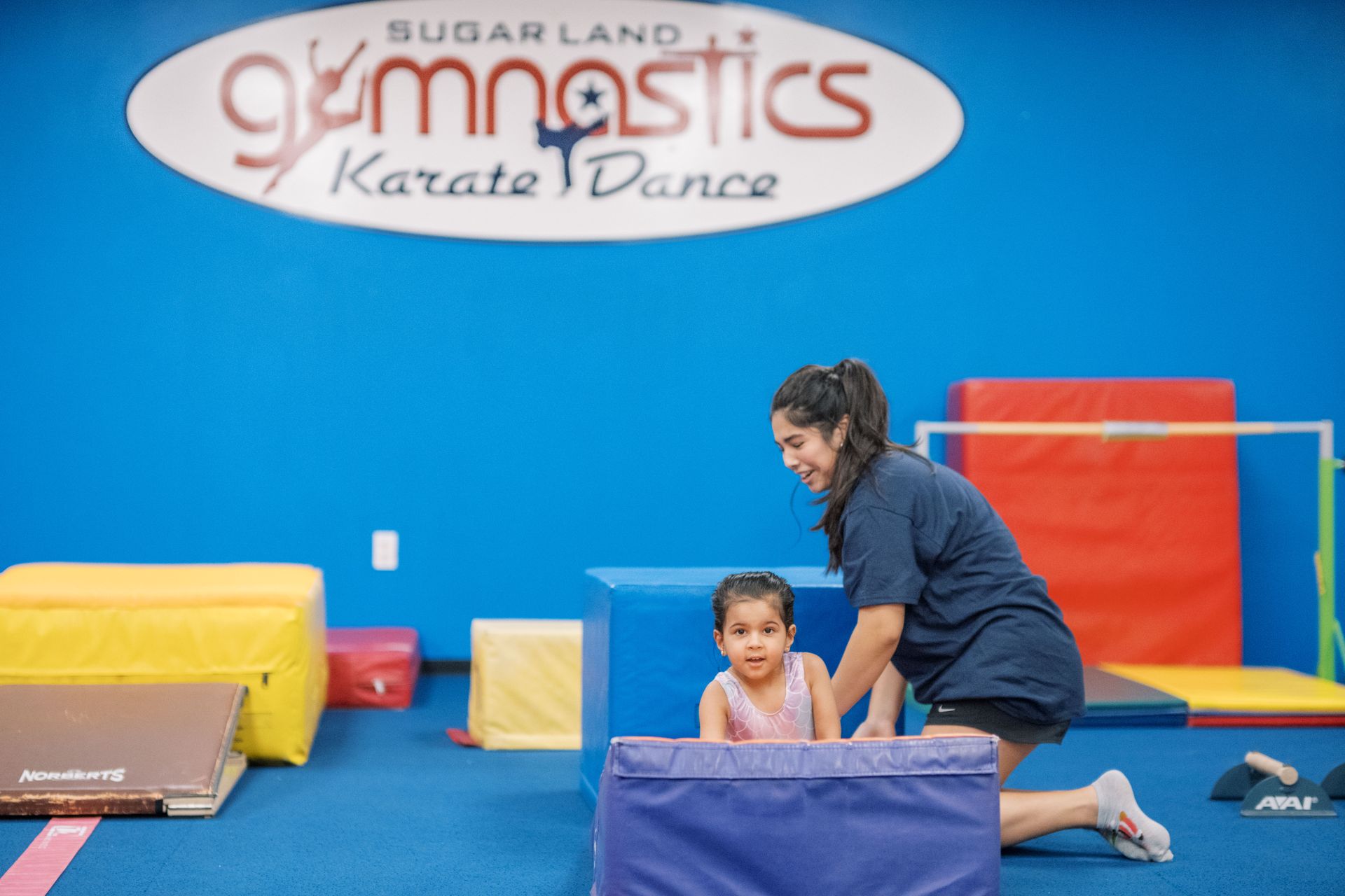 A woman is helping a little girl do exercises in a gym.