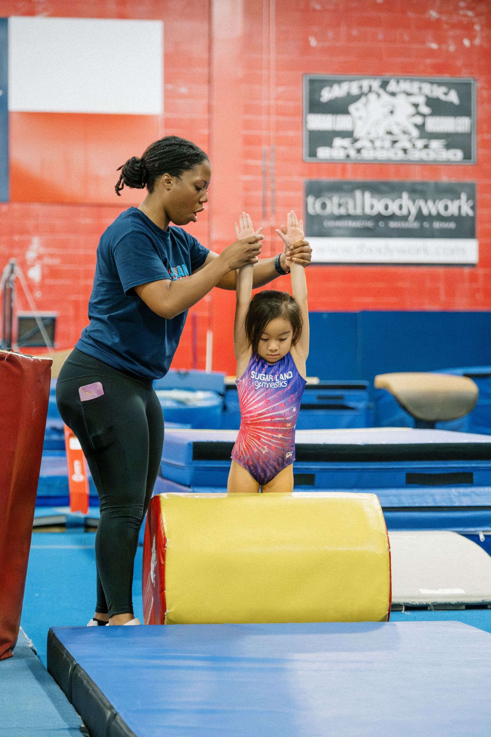 A woman is helping a little girl do gymnastics in a gym.
