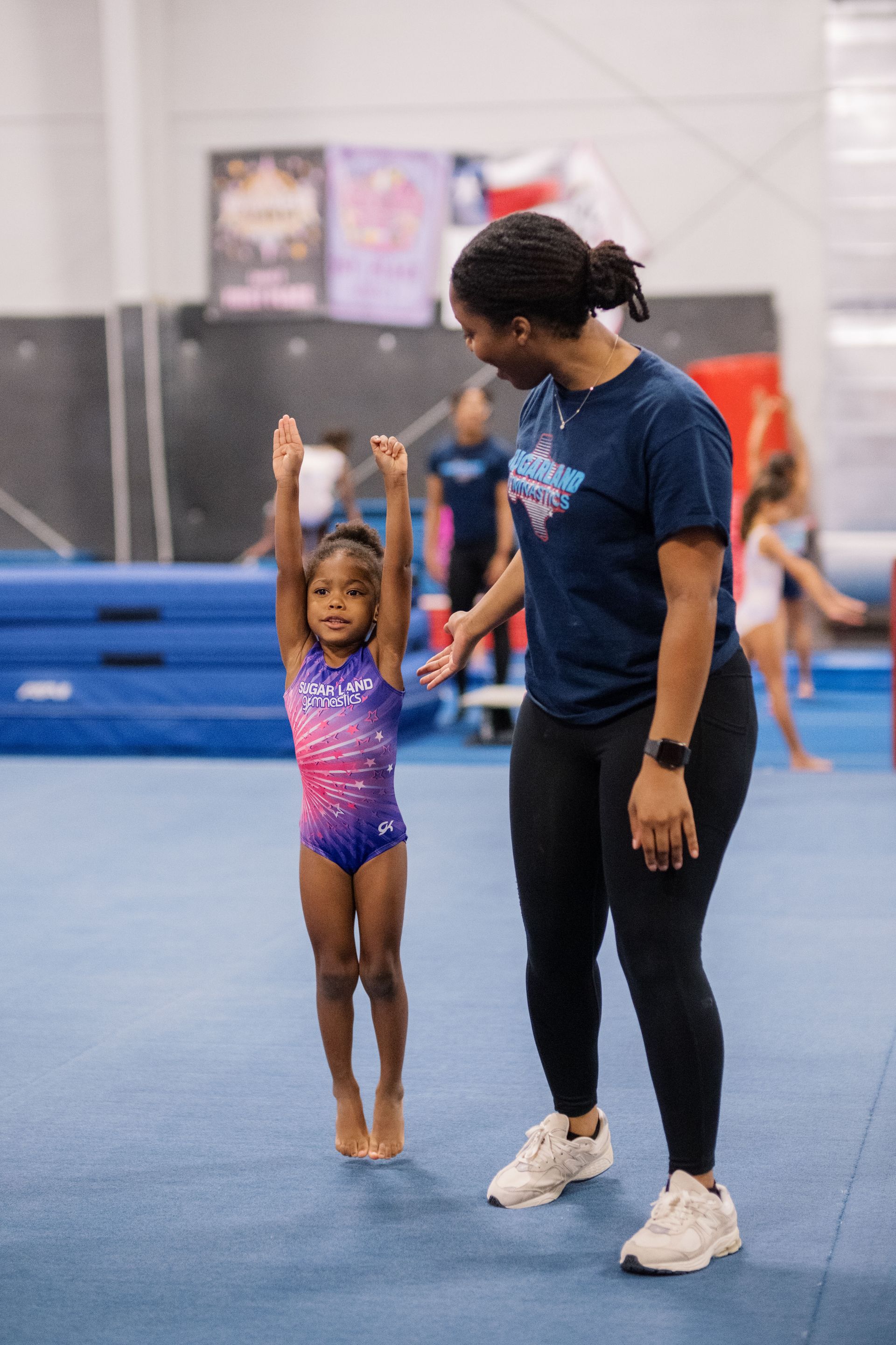 A woman is standing next to a little girl on a gym floor.