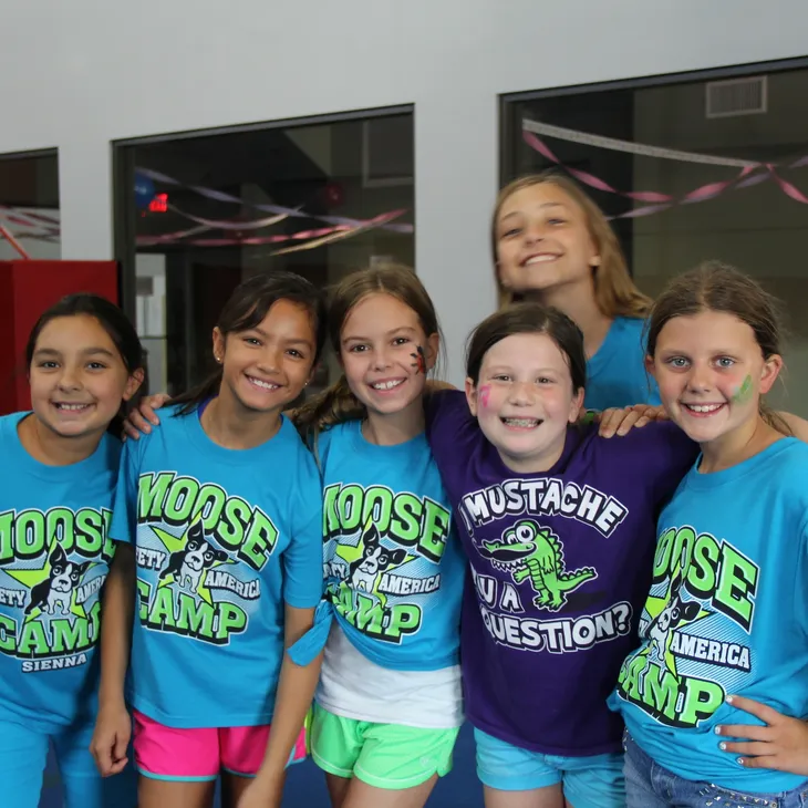 A group of young girls wearing moose camp shirts pose for a picture