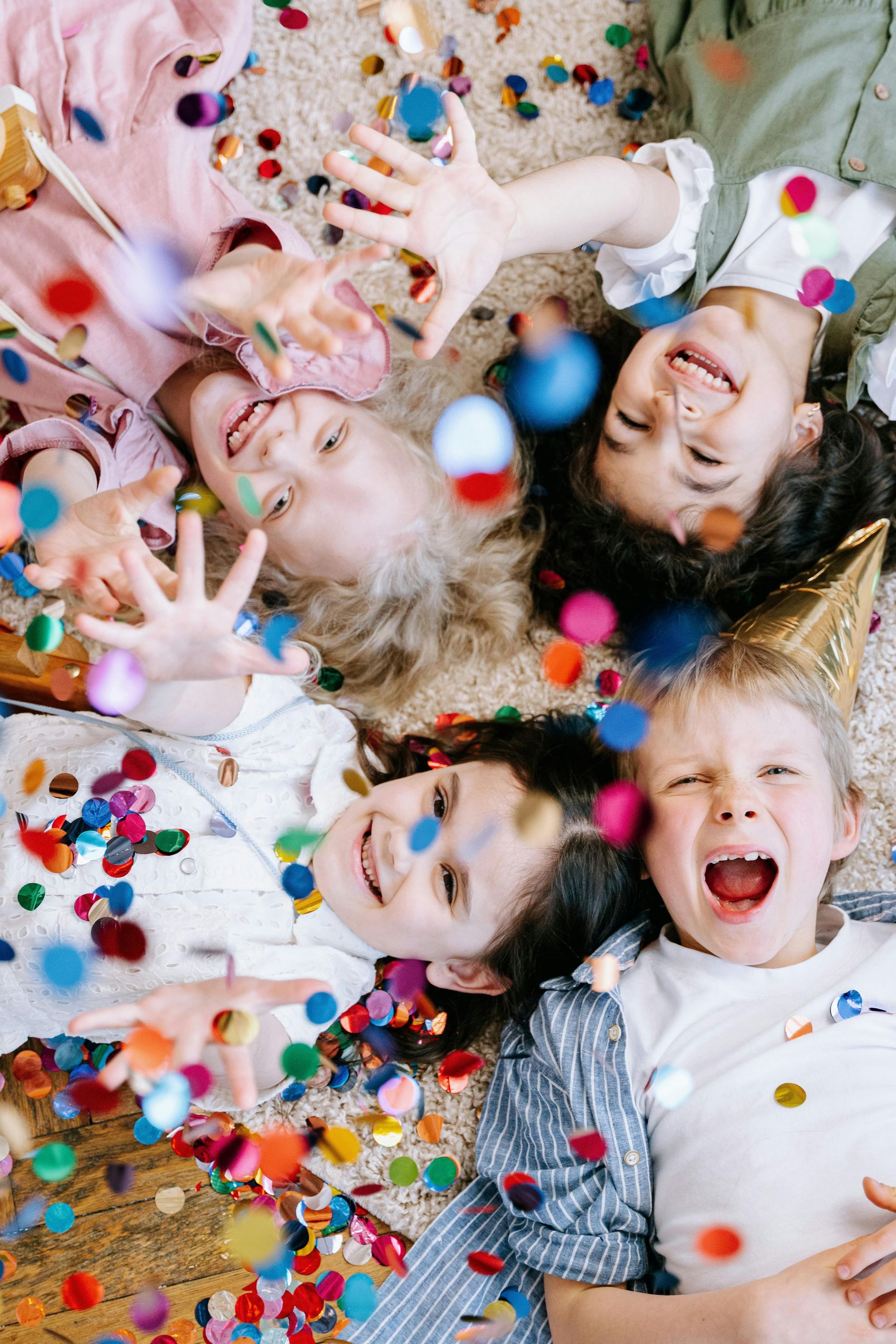 A group of children are laying on the floor covered in confetti.