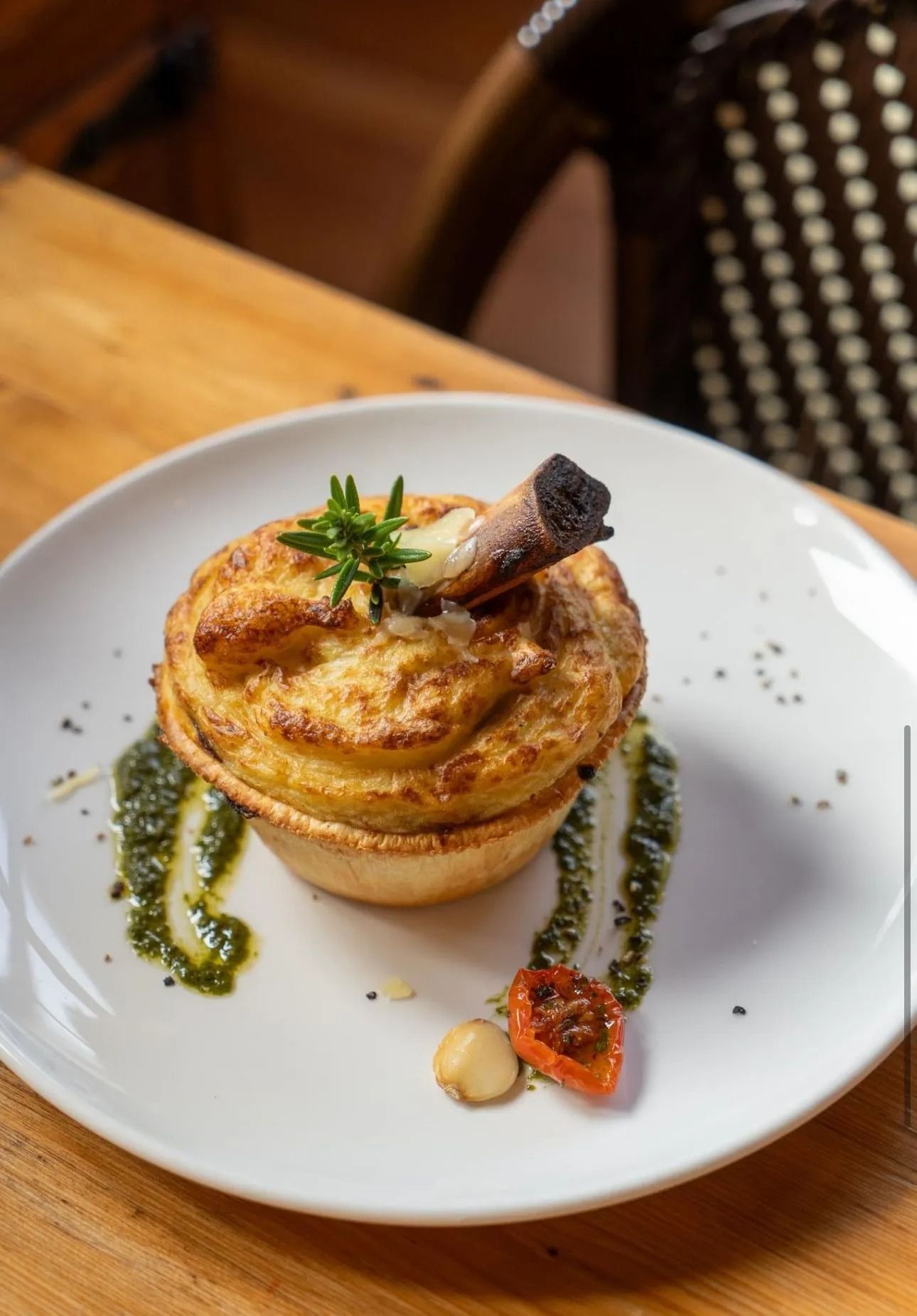 A golden-brown meat pie with a protruding bone, garnished with a sprig of rosemary, served with pesto on a white plate. — 321 Cafe Learmonth In Learmonth, VIC