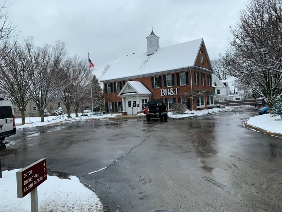 A stone pathway leads to the front door of a two-story home, flanked by lush green trees, shrubs, and colorful flowers.