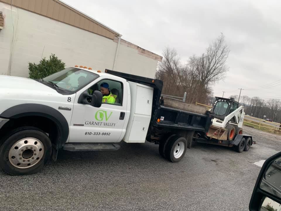 A close-up view of a transition between light gray concrete pavers and a walkway made of textured, reddish-brown bricks.