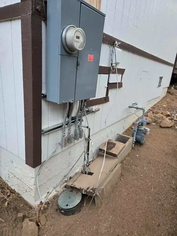 Gray electrical panel on a white house, with conduits, meter, and gas line.