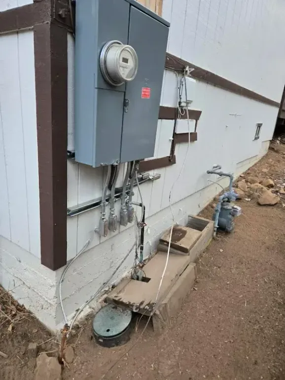 Gray electrical panel on a white house, with conduits, meter, and gas line.