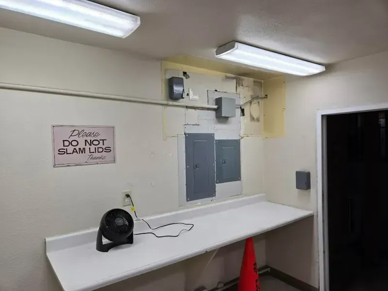A small room with electrical panels, a workbench, and a sign that says 