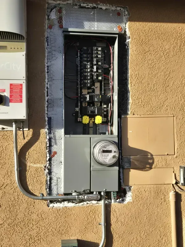 Electrical panel installed on a stucco exterior wall; includes a meter, breakers, and conduit.