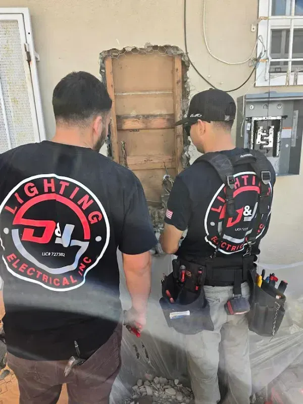 Two electricians work outside a building, fixing a wall opening.