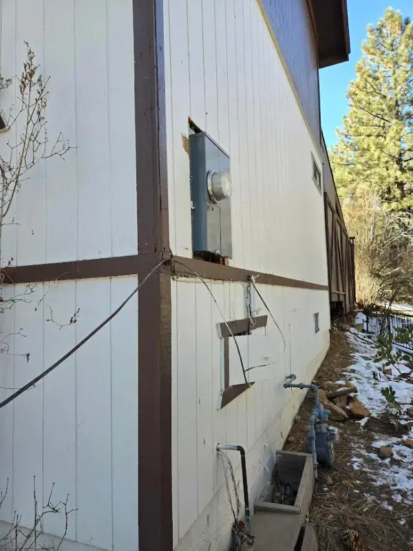 Side of a white house with brown trim, a gray electrical box, and wire. Exterior view.