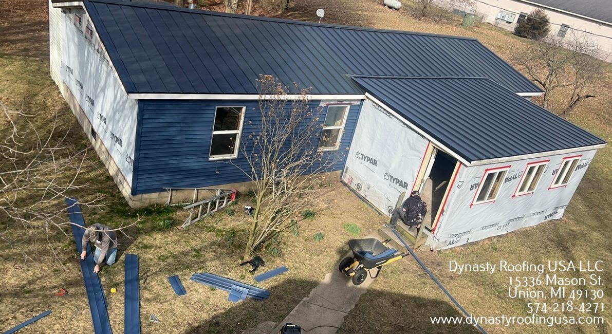 House with blue siding and dark blue metal roof under construction. Two workers.