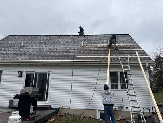 Workers replacing a shingle roof with a metal roof on a white house roof, with ladders and roofers visible.